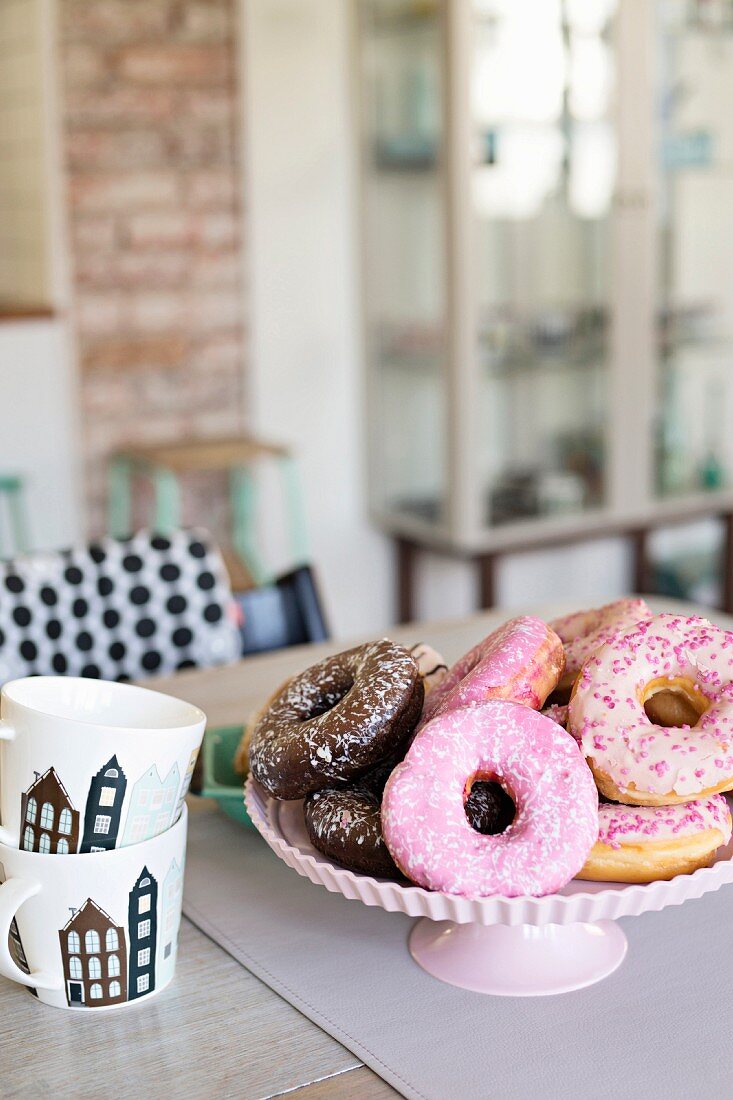 Donuts mit Zuckerguss auf Gebäckständer und gestapelte Kaffeebecher