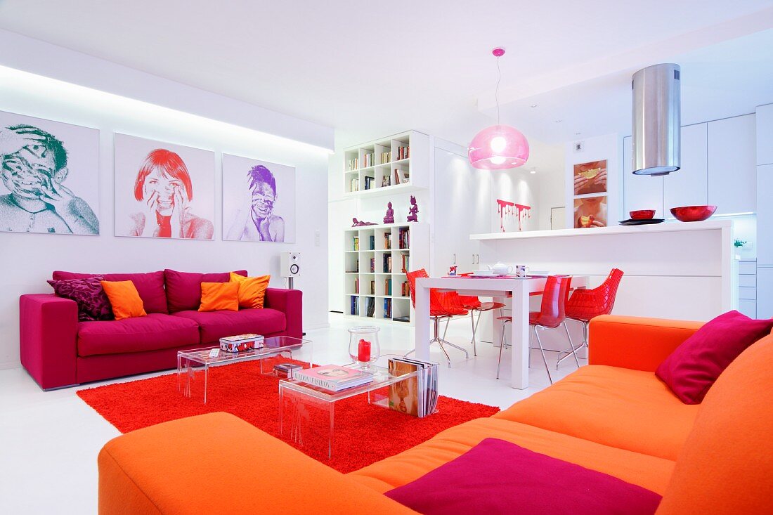 Open-plan living area in shades of bright red and orange with green, red and purple portraits on wall