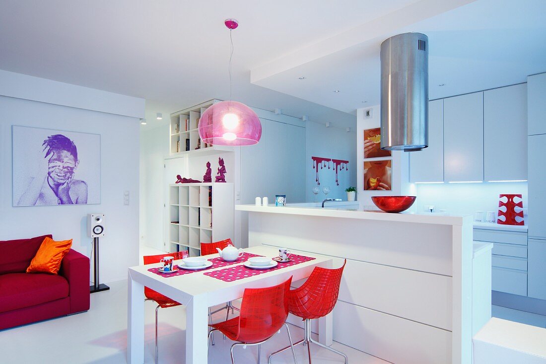 Rote Schalenstühle an Esstisch vor weißer Küchentheke in offenem Wohnraum