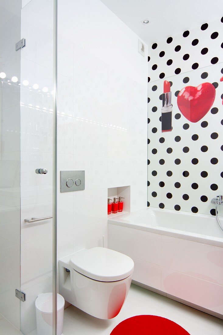 Toilet next to bathtub in white bathroom with polka-dot wall