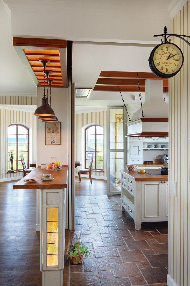 Open-plan interior with counter in foreground, kitchen with vintage station clock and lounge area with tall, lattice windows in background