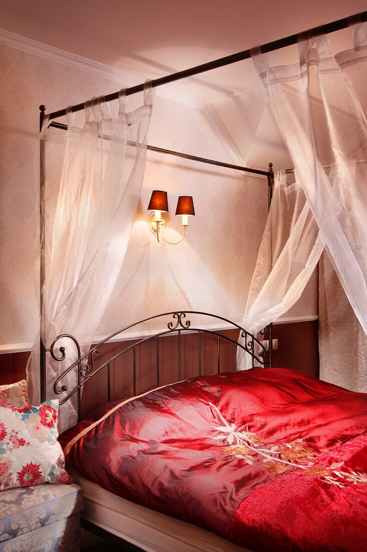 Four-poster bed with curved, metal headboard, transparent canopy and red, satin bed linen