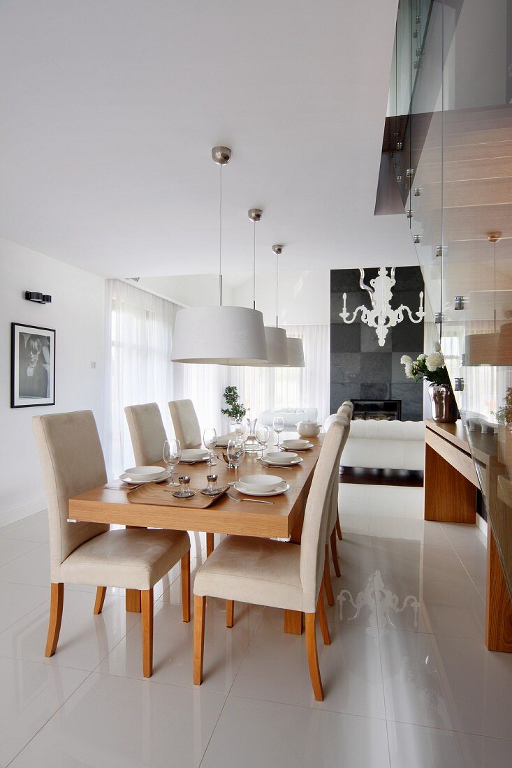 Set dining table, pale, upholstered chairs and pendant lamps with white lampshades in open-plan interior