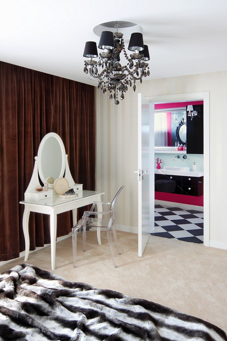 Weisser Schminktisch mit Spiegelaufsatz in postmodernem Stil und Ghost Stuhl vor braunem Vorhang, offene Tür und Blick ins Bad