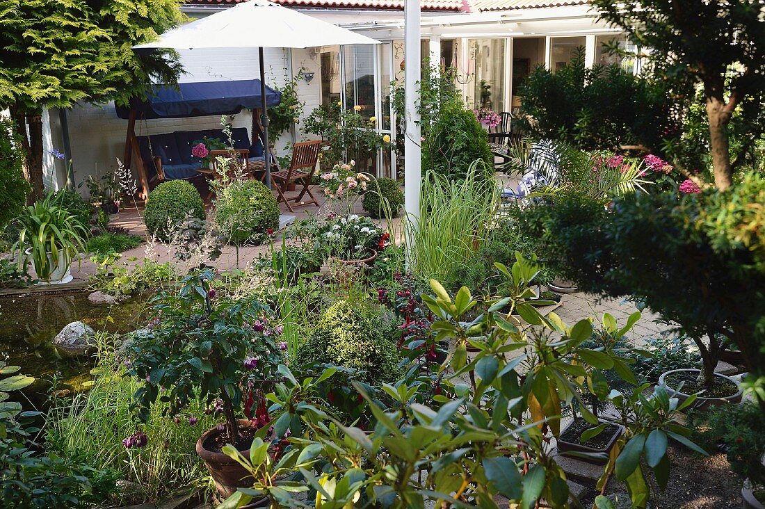 Lauschiger Terrassenplatz mit blauer Hollywoodschaukel und weißem Sonnenschirm in Garten mit Teich