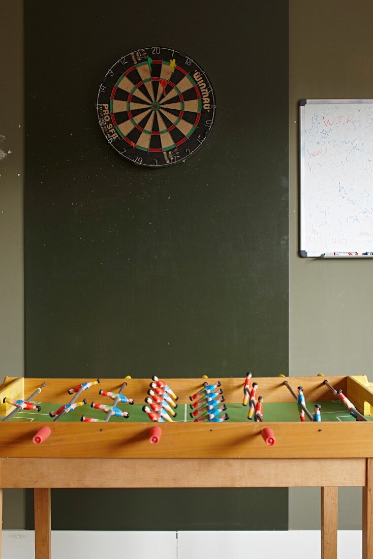 Dartboard on dark green wall behind table football set