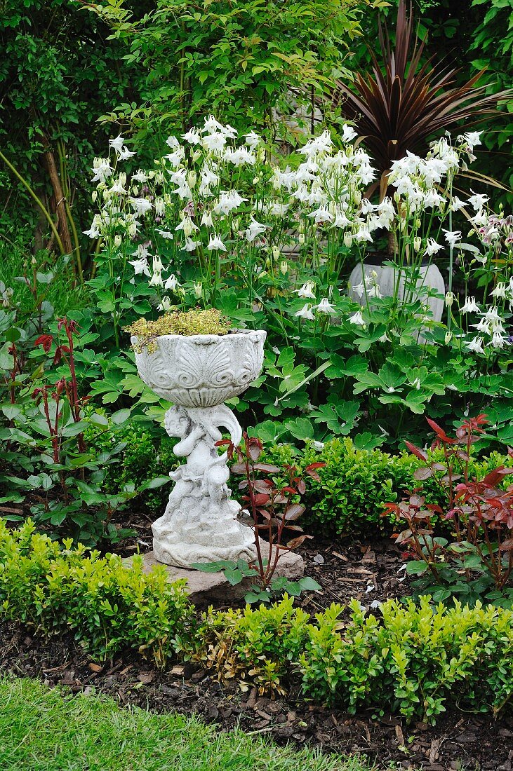 Pflanzgefäss mit Figur in blühendem Garten