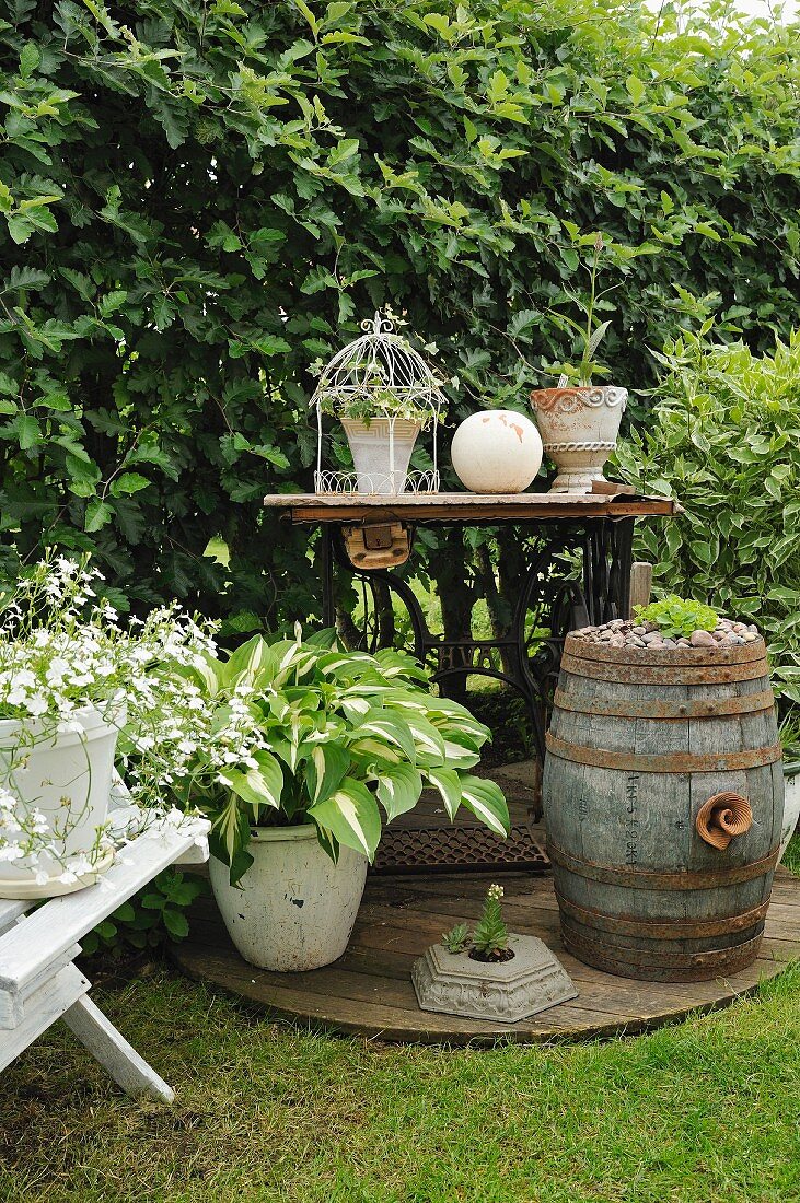 Nostalgic arrangement of planted, rustic barrel and ornaments on vintage sewing machine table in corner of garden