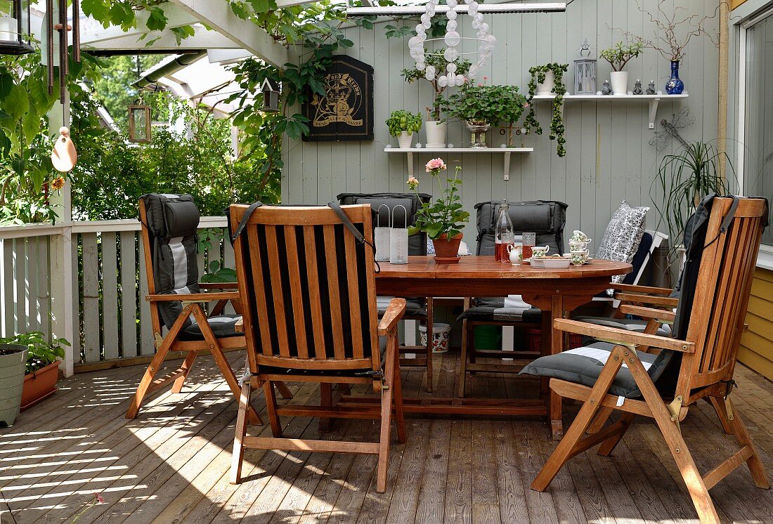 Wooden chairs with black seat cushions around table on veranda with wooden floor