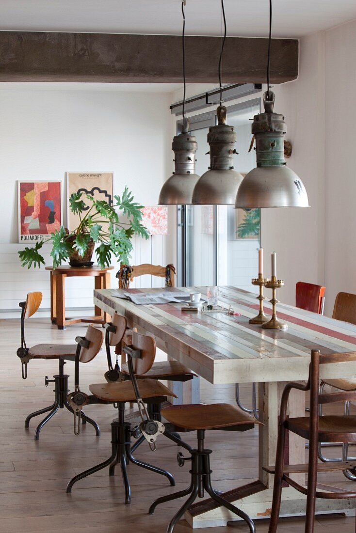 Retro Drehstühle an langem Tisch mit Industrie-Pendelleuchten in Loft-Wohnung