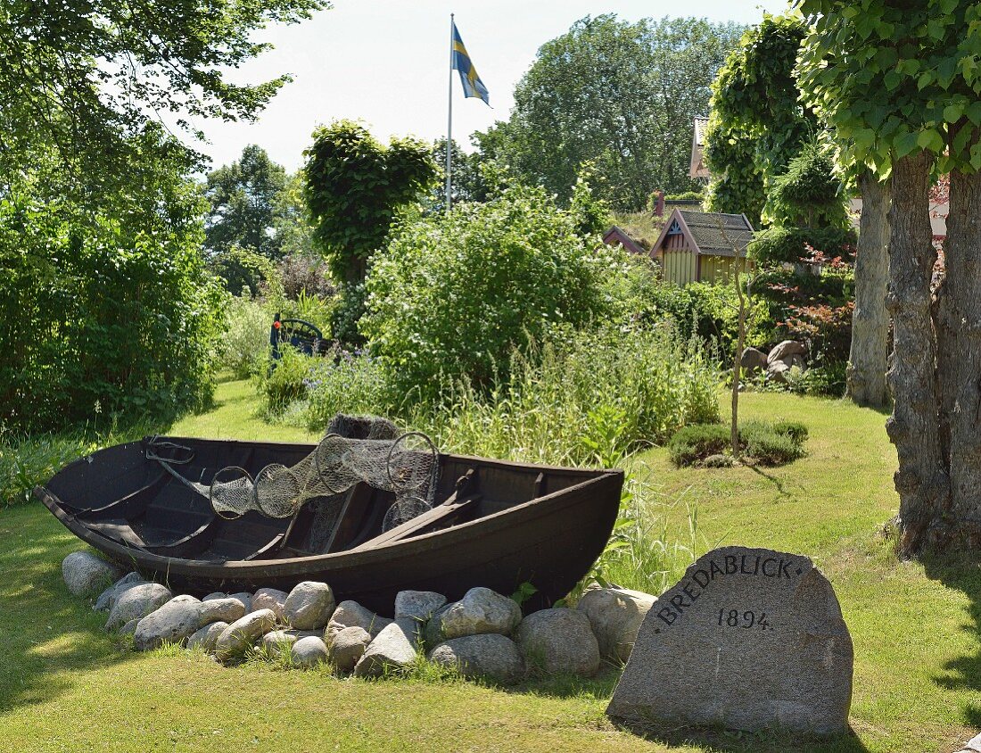 Traditional wooden rowing boat resting on rocks in summer garden