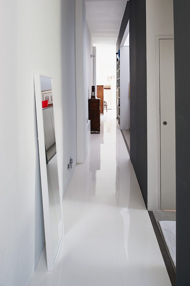 Narrow hallway with white, resin floor and full-length mirror leaning against wall