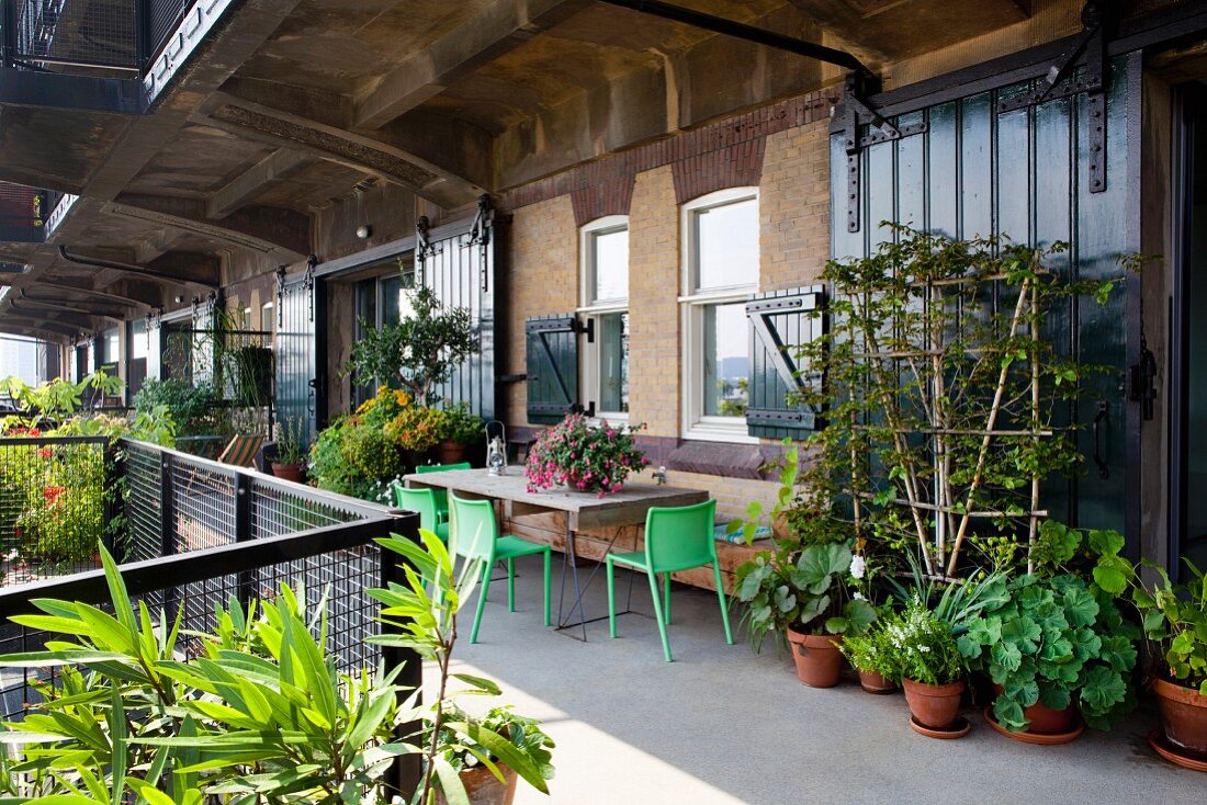 Üppig begrünter urbaner Balkon mit verschiedenen Pflanzentöpfen und Sitzplatz vor Loftfassade