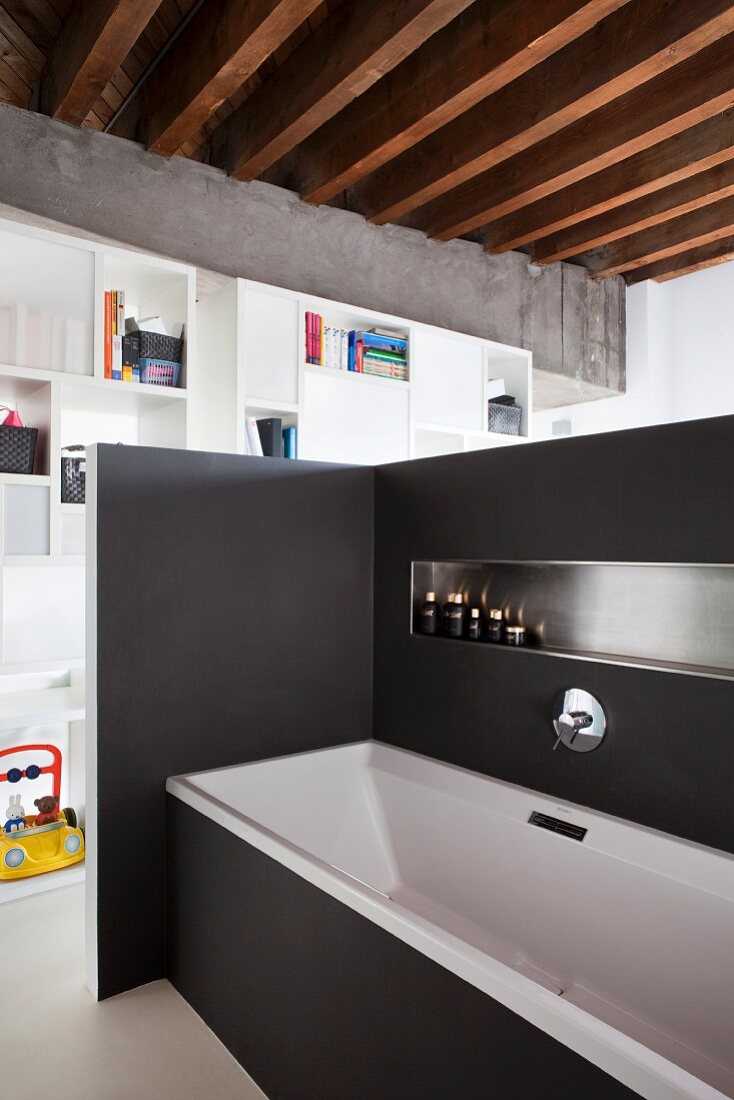 Badewanne an schwarzer Raumteilerwand mit eingebauter Ablage, im Hintergrund offenes weisses Regal als Raumteiler in Loftwohnung