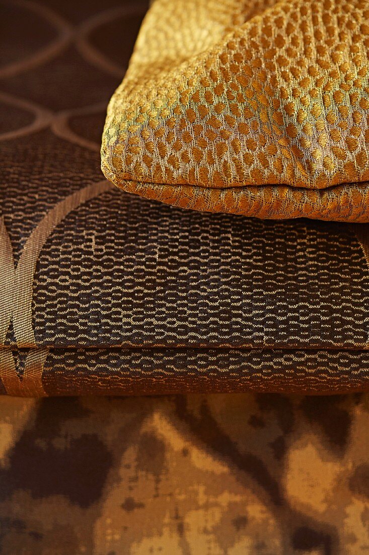 Gold, spotted cushion on folded blanket with ethnic pattern