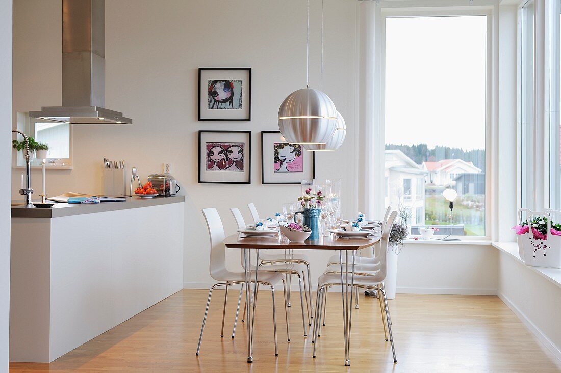 Gedeckter Tisch und moderne Stühle unter Designer-Pendelleuchten vor Kücheninsel mit Dunstabzug