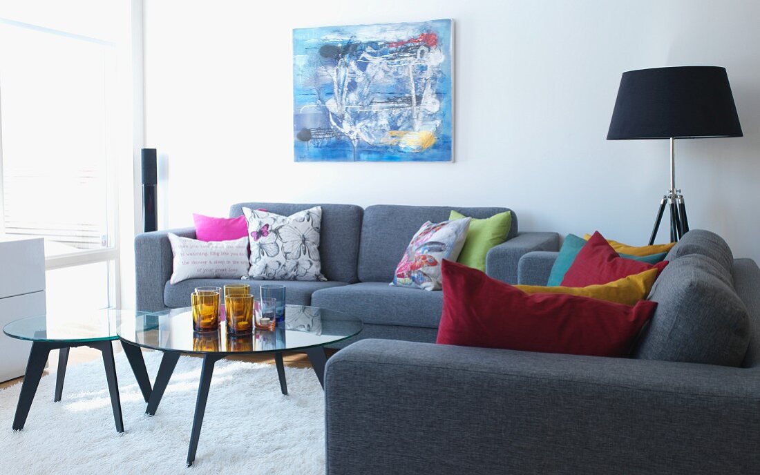 Graue Sofagarnitur mit farbigen Kissen um Couchtischset mit Glasplatte in modernem Wohnzimmer