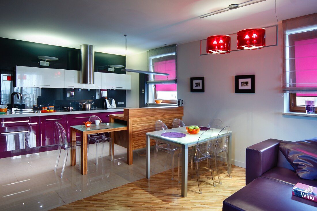 Offener Wohnraum, Essplatz mit Ghost Stühlen vor Theke aus Holz und ausziehbarer Küchentisch, im Hintergrund moderne Einbauküche mit violetten und schwarzen Farbakzenten