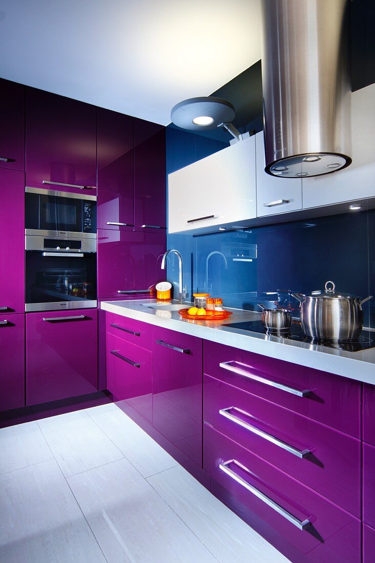 Moderne Einbauküche mit violetten Schrankfronten, im Vordergrund Edelstahl Dunstabzug
