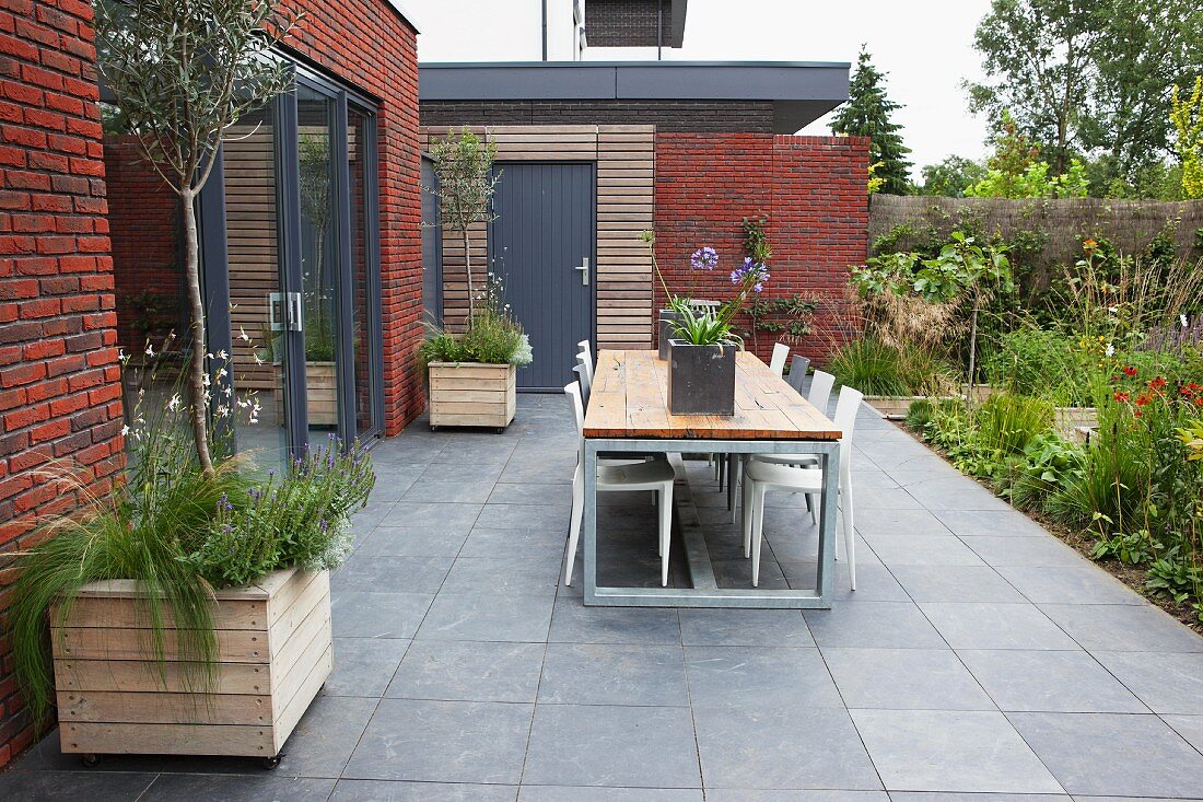 Table and chairs on terrace with grey floor tiles adjoining modern, brick extension