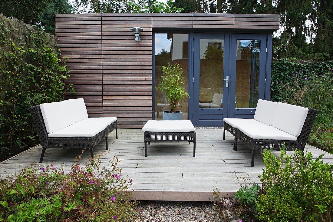 Outdoor furniture with dark frames and white seat cushions on terrace adjoining contemporary summer house