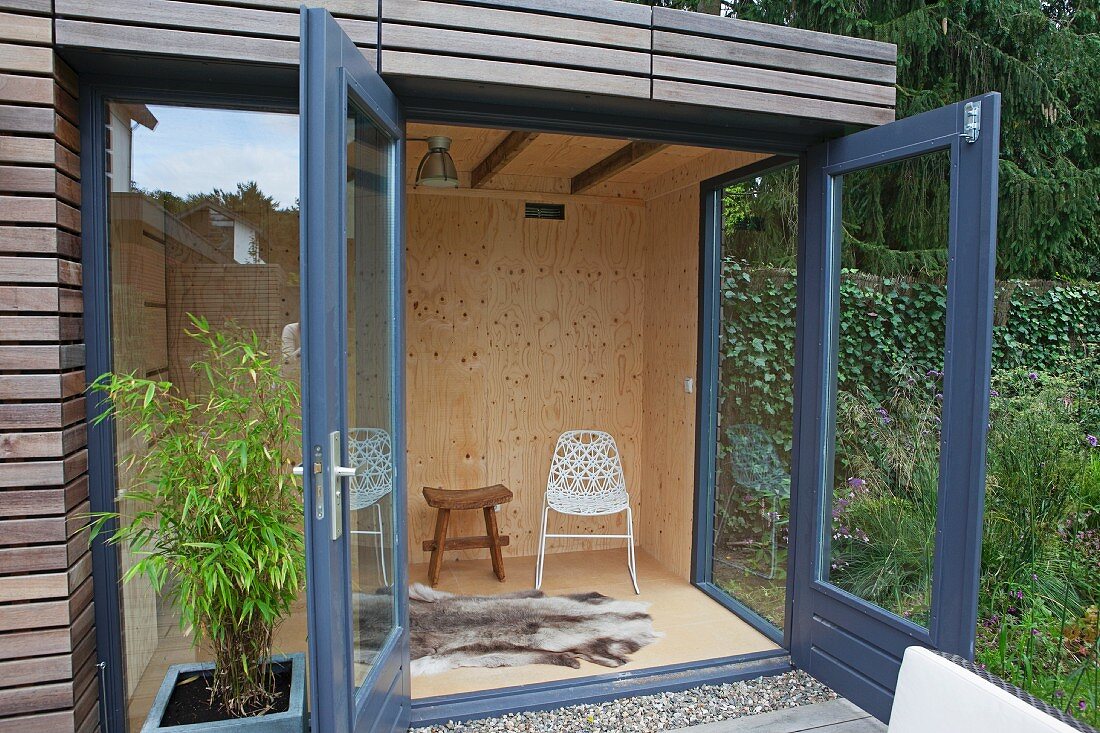 Offene Terrassentür eines bewohnbaren Gartenhäuschens, Blick in Innenraum auf Tierfell am Boden und verschiedene Sitzmöbel