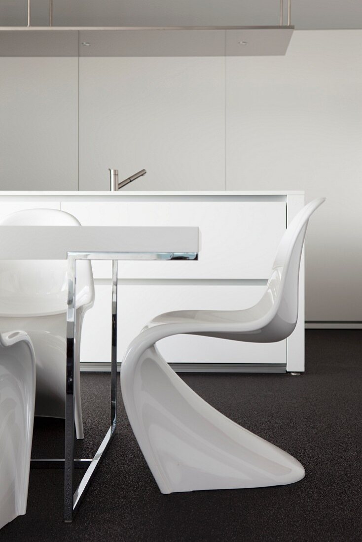 Weißer Panton Chair am Tischchromgestell, im Hintergrund freistehende Designer-Küchentheke