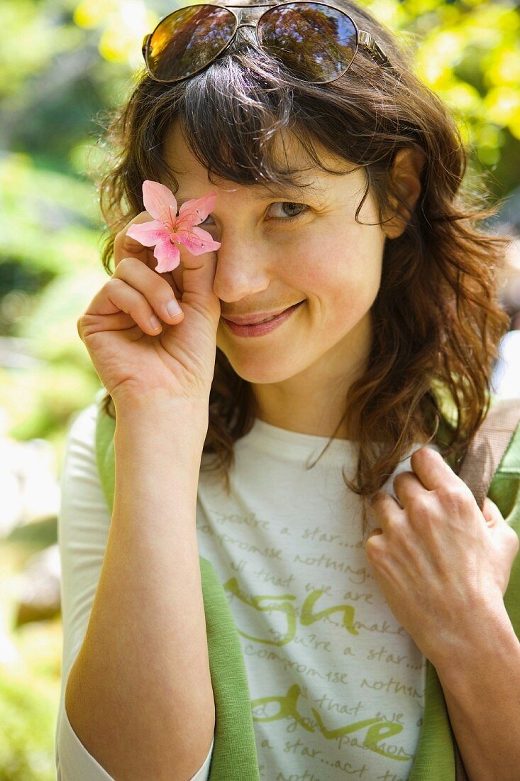 Junge Frau hält eine rosa Blüte vor das Auge