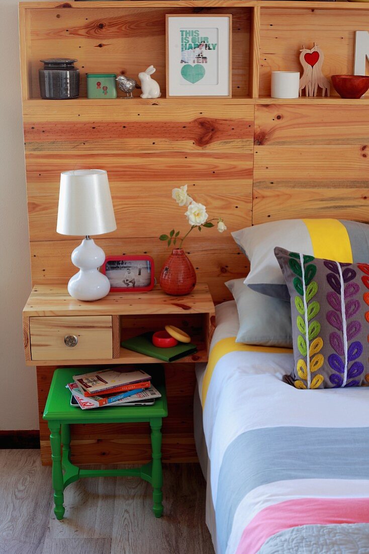 Holzelement mit jugendlich dekorierten Regalfächern und Nachtkästchen als Kopfteil eines Doppelbetts mit gestreiftem Bezug und bunten Kissen