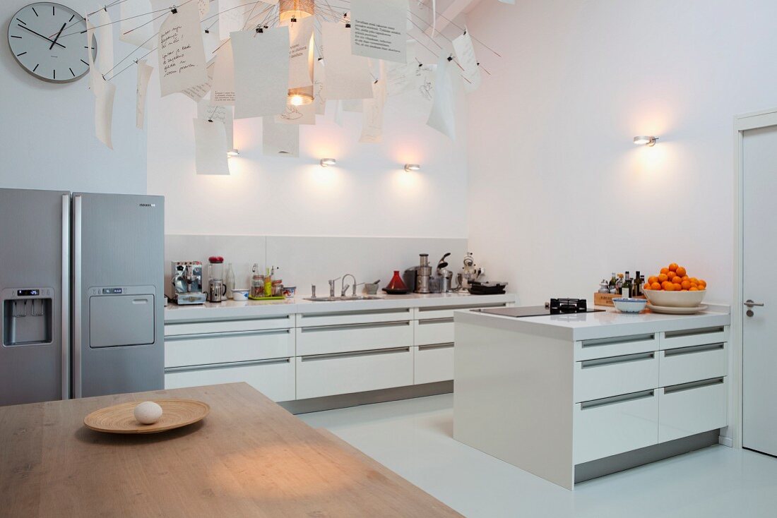 Blick über Esstisch in offene, weiße Designerküche, an der Seite Edelstahl Kühlschrankkombination