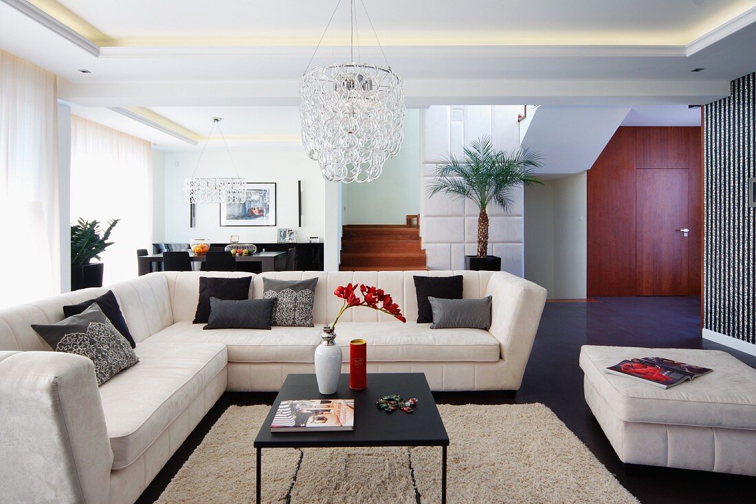 Elegant, pale corner couch and coffee table on flokati-style rug in open-plan interior with indirect ceiling lights