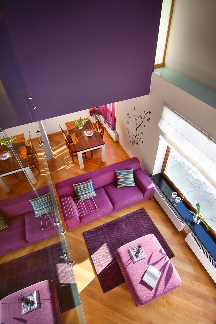 Blick von Galerie auf pinkfarbenes Sofa und Polsterhocker als Tisch, auf diagonal verlegtem Parkettboden in zeitgenössischem Wohnhaus