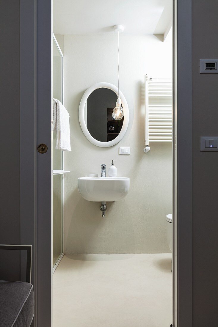 Blick durch graue Schiebetüröffnung in weißes Bad mit ovalem Wandspiegel und Waschbecken