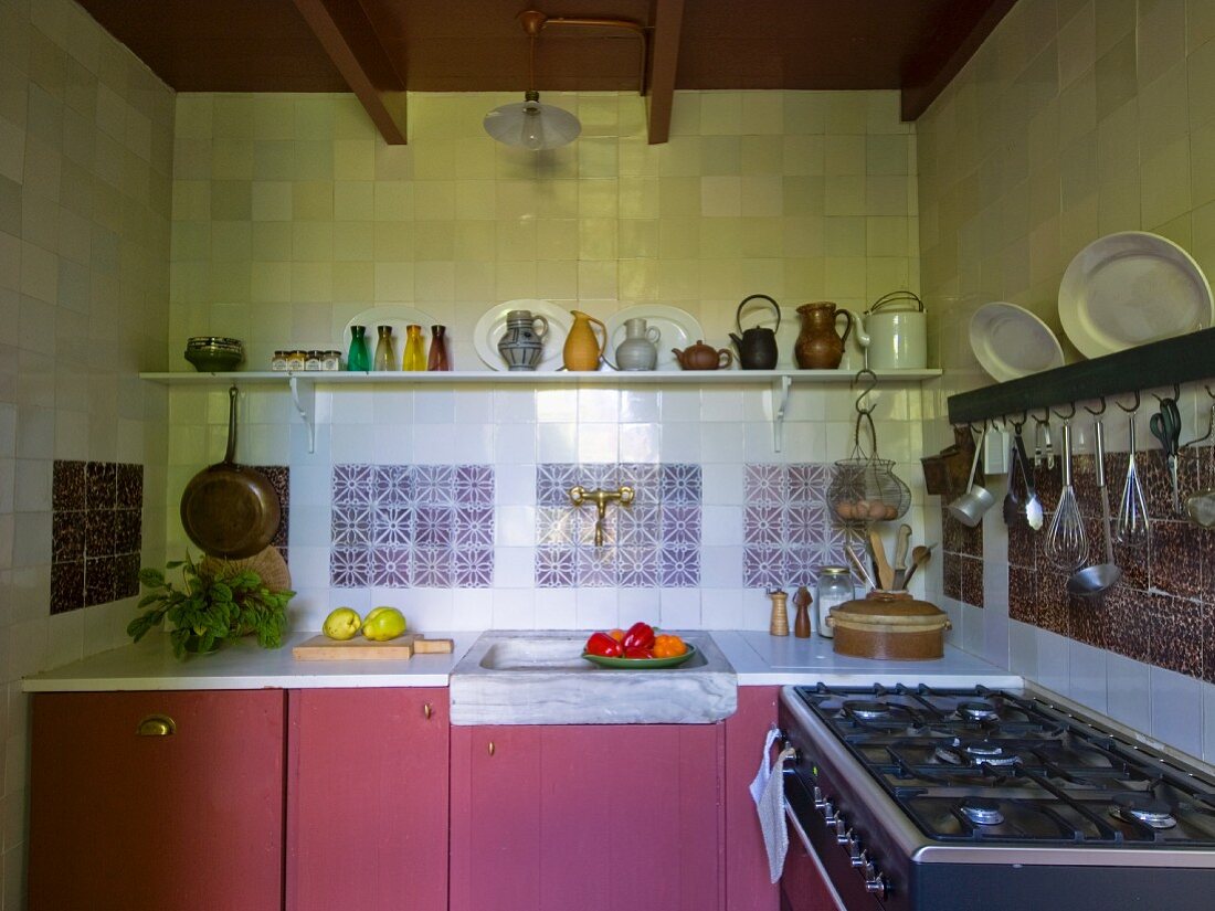 Kitchen counter with dusky-pink base units below shelf of jugs on tiled wall