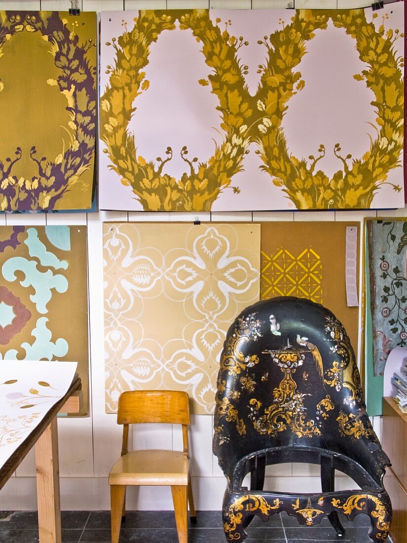 Child's chair and armchair with gilt ornamentation against wallpaper designs on wall of studio
