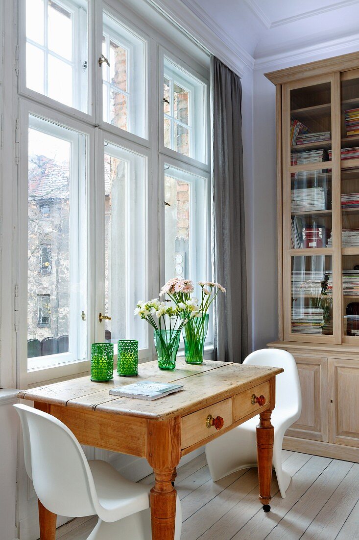 Wooden table with drawers and white Panton chairs in front of bookcase in traditional, period interior