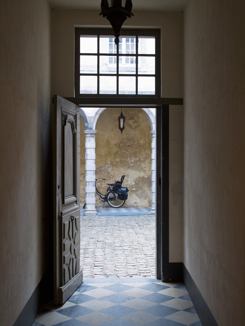 Historischer Hauseingang mit Schachbrettmuster Bodenfliesen in Diagonalverlegung, offene Tür und Blick auf gepflasterten Innenhof