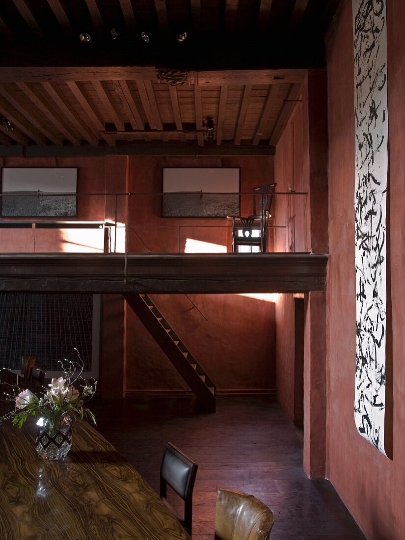 Rustikaler Wohnraum rotbraun getönt mit langer künstlerischer Papierfahne, im Hintergrund Lichteinfall auf Galerie und Holzstiege