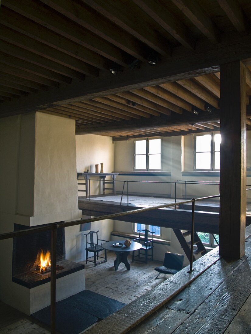 Blick von Galerie auf Kaminfeuer in reduziertem restauriertem Wohnraum mit Holzdecke und rustikalem Flair