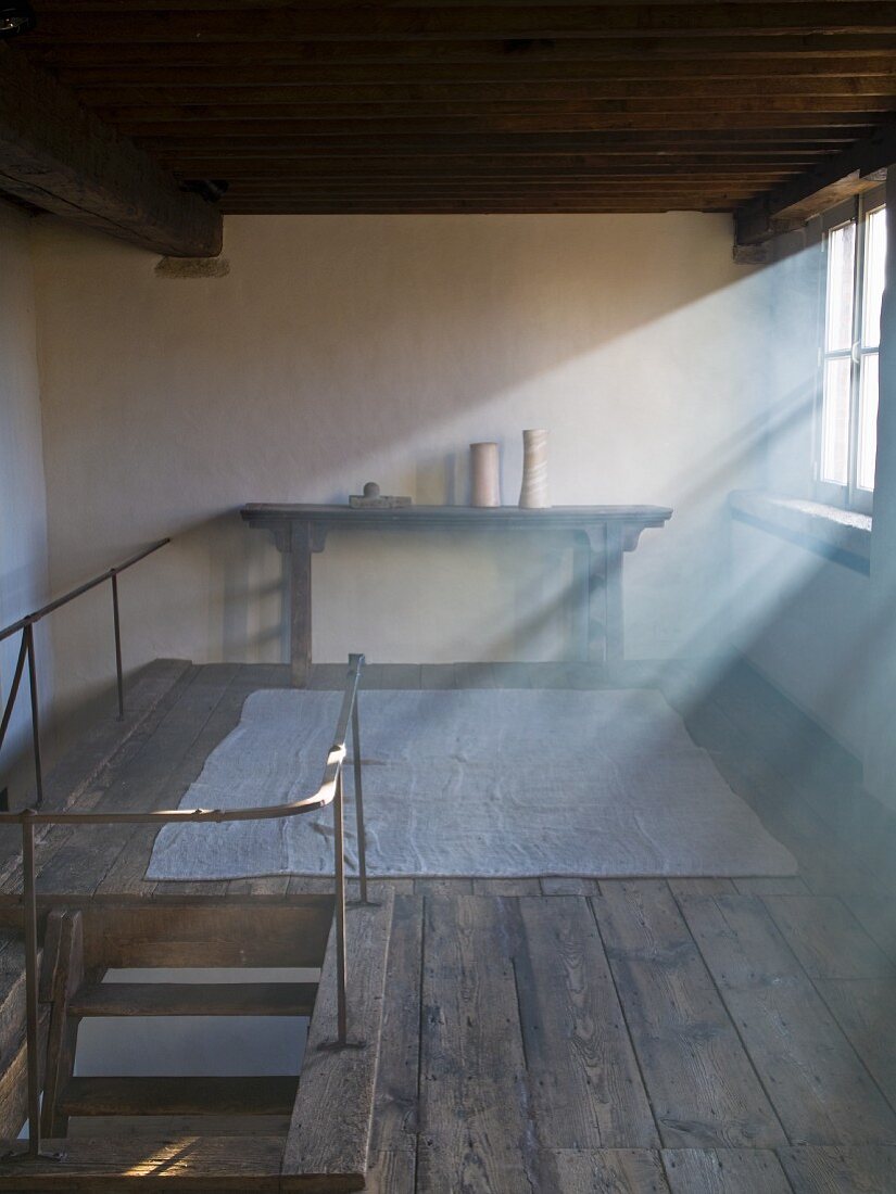 Lichteinfall durch Fenster auf restaurierte Galerie, rustikaler Dielenboden mit antikem Wandtisch