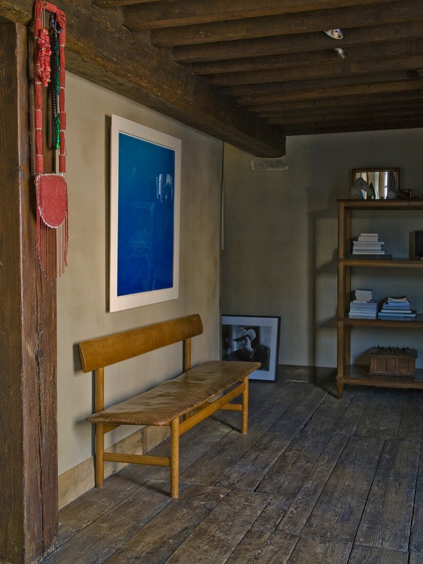 Schlichte Retro Sitzbank auf rustikalem Dielenboden in restauriertem Raum mit Holzbalkendecke und modernem blauem Bild