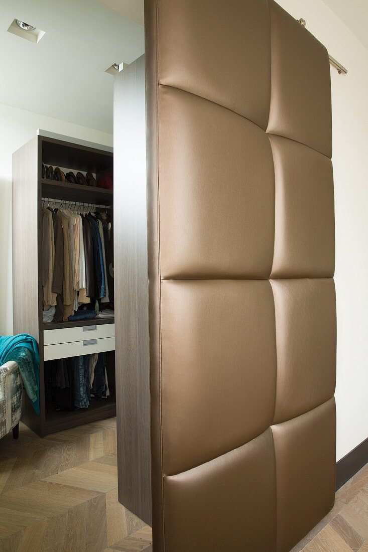 Open, upholstered sliding door with brown, shimmering cover and view into dressing room