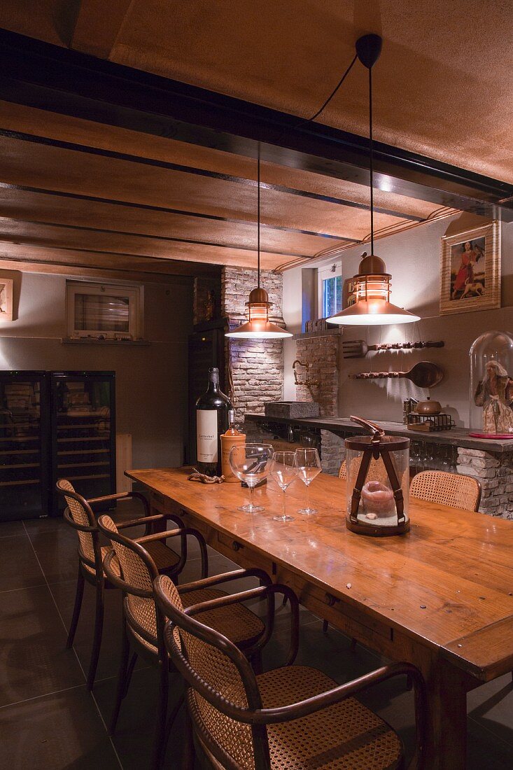 Thonet armchairs around rustic wooden table below retro, pendant lamps hanging from ribbed ceiling in wine cellar