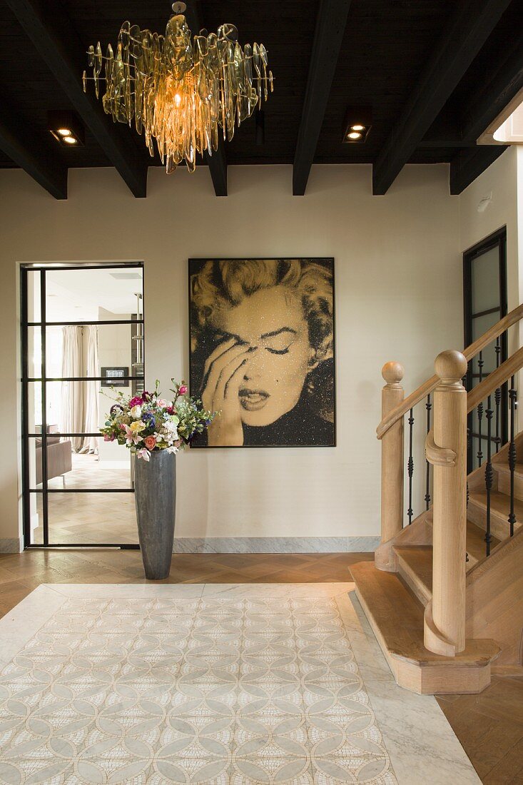 Entrance hall with extravagant pendant lamp hanging from wooden ceiling, portrait of Marilyn Monroe on wall and bouquet in floor vase