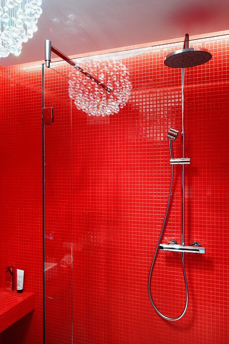 Kopf- und Handbrause an rot gefliester Wand einer Dusche, Spiegelung der Pendelleuchte