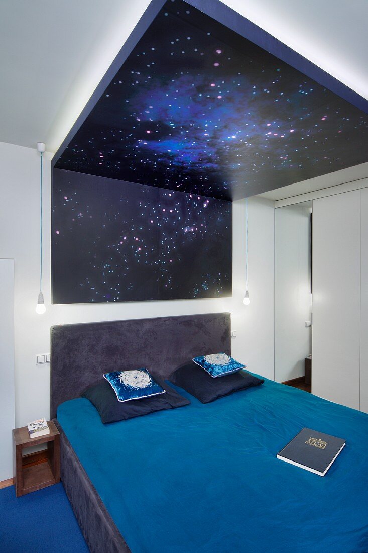 Doppelbett mit blauer Bettwäsche unter Sternenhimmel, hinterleuchtetes, bedrucktes Glas an Decke und Wand, in modernem Schlafzimmer