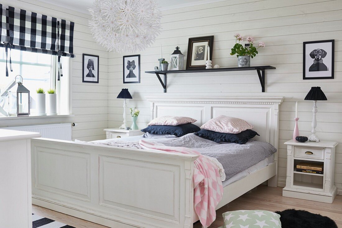 Weisses, antikes Holzbett vor Holzwand mit schwarzem Reagalbord, Nachtkästchen mit Tischlampen in ländlichem Schlafzimmer