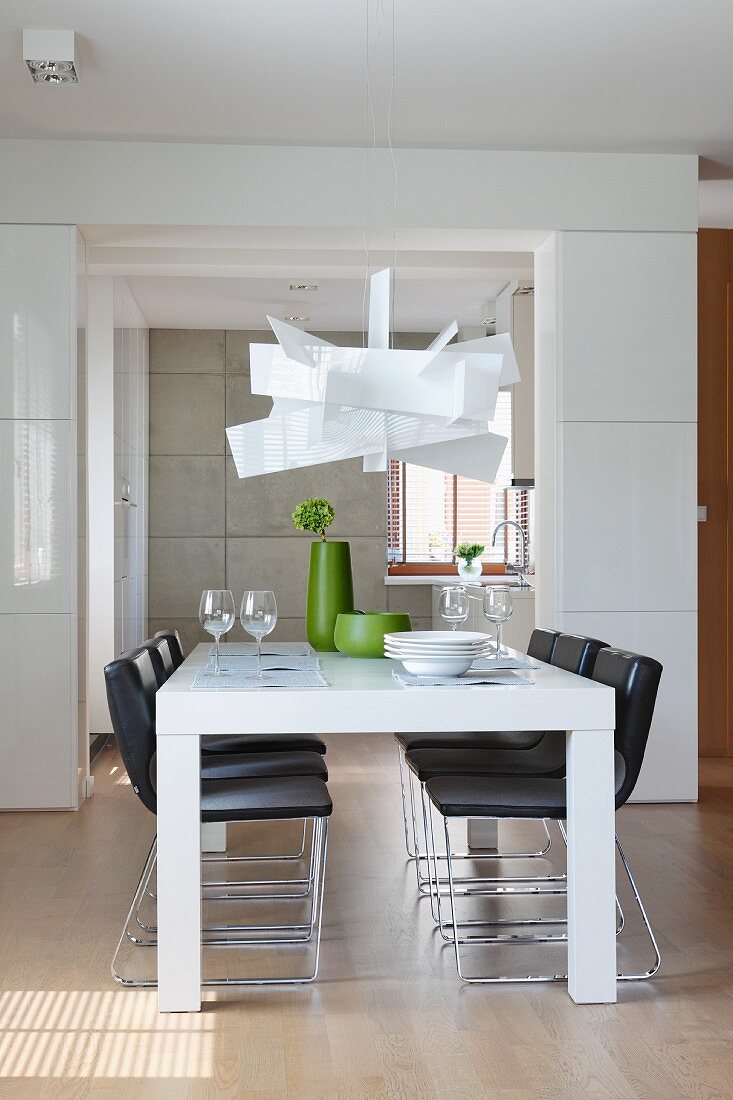 Designerlampe über weissen Esstisch und schwarze Stühle in offenem Wohnraum