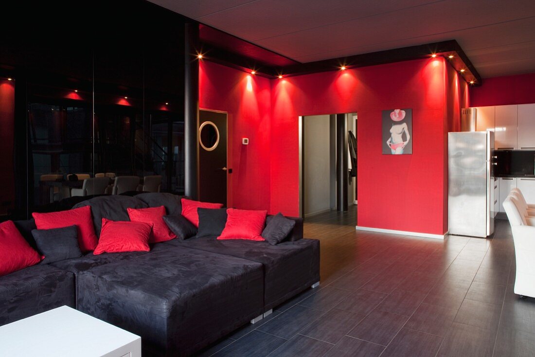 Sofa combination against dark, reflective wall and red wall with ceiling spotlights in loft apartment