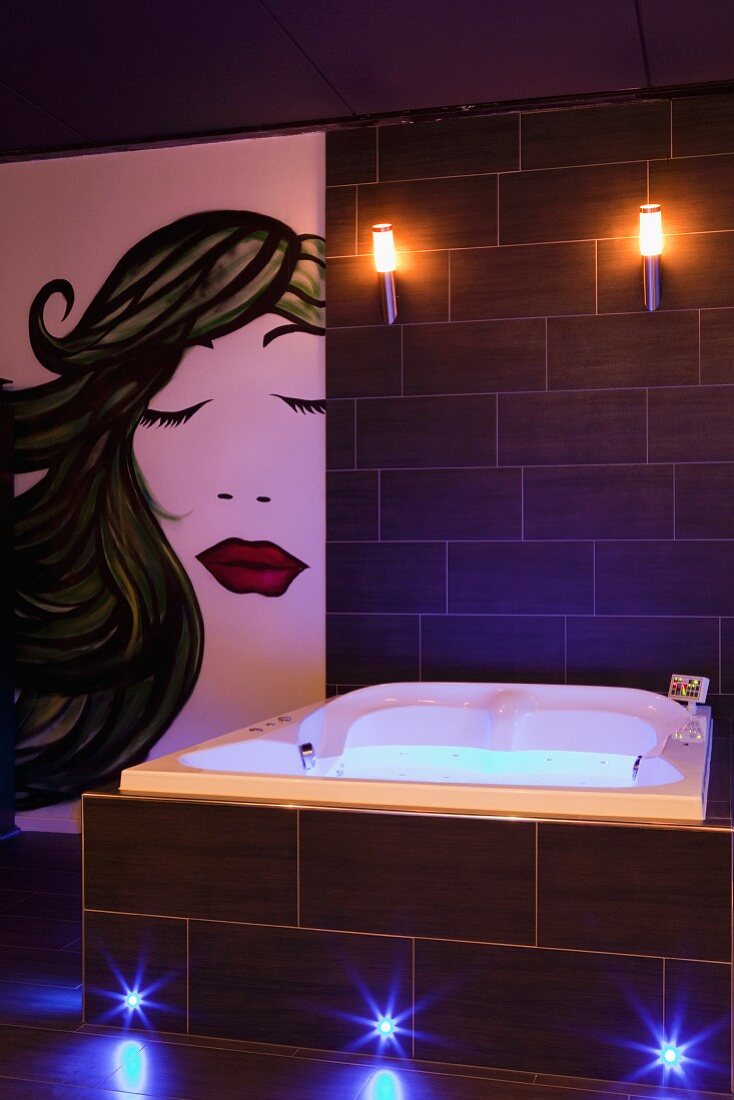 Wandmalerei im Stil der Popart neben beleuchtetem Whirlpool in schwarz gefliestem Badbereich
